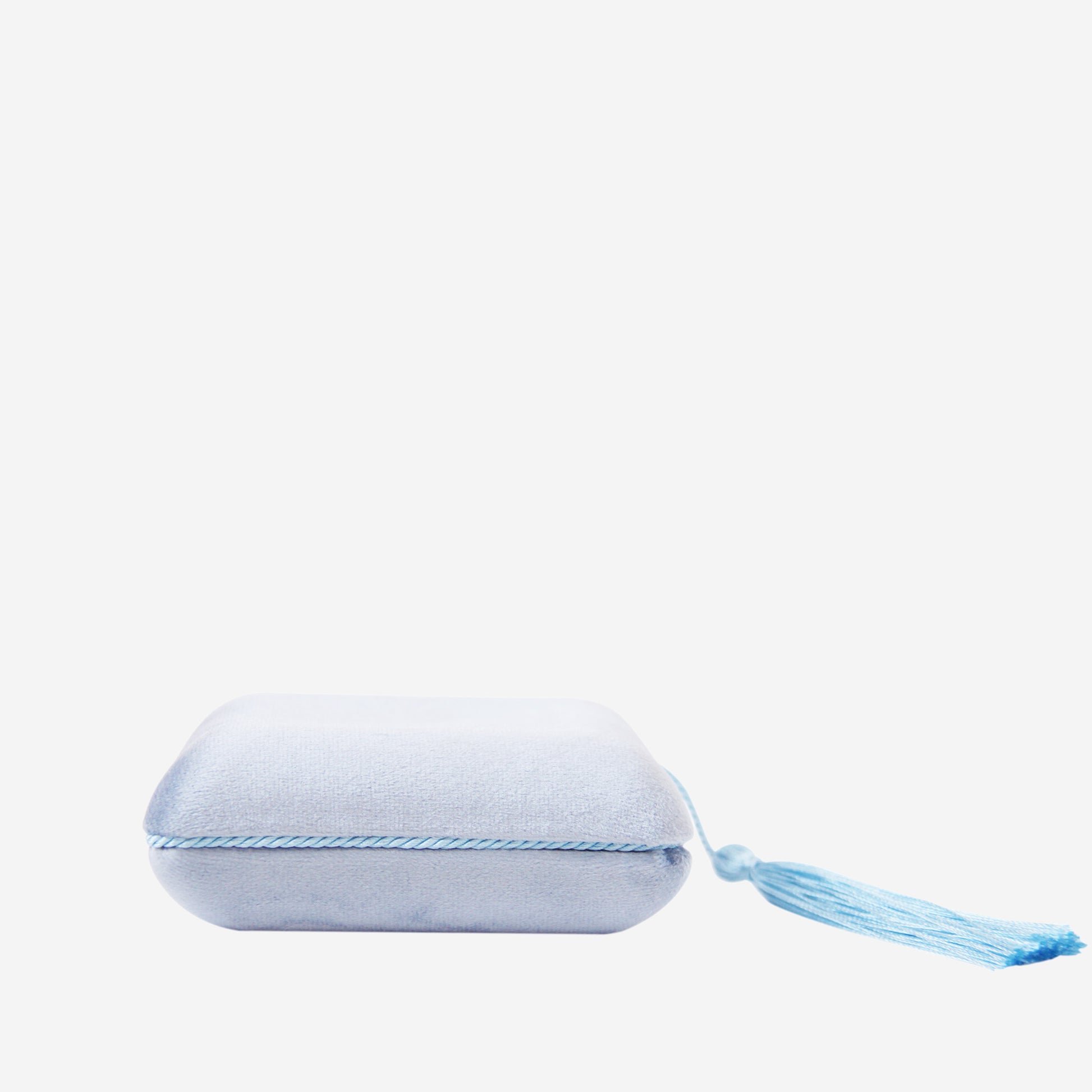 Closed blue velvet jewellery box with tassel detail on an off white background