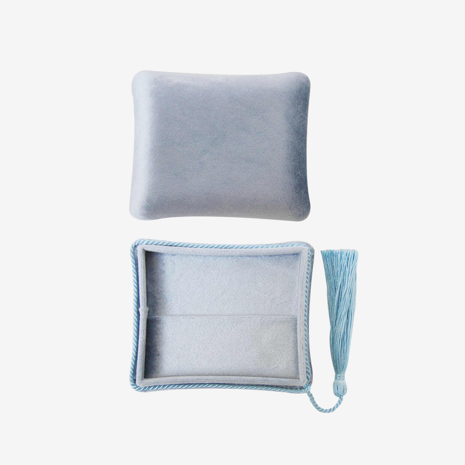 Open blue velvet jewellery box with tassel detail on an off white background