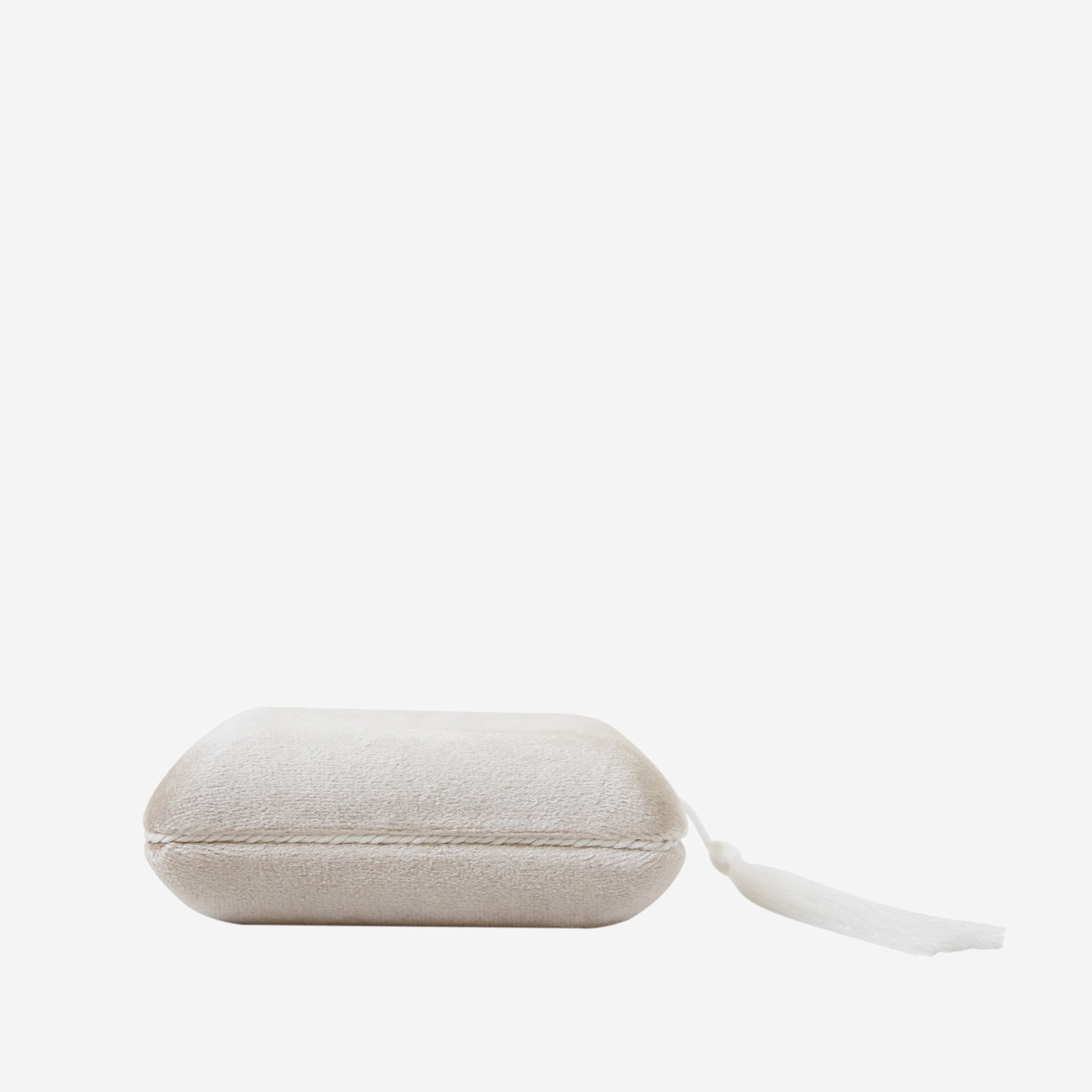 Closed champagne velvet jewellery box with tassel detail on an off white background