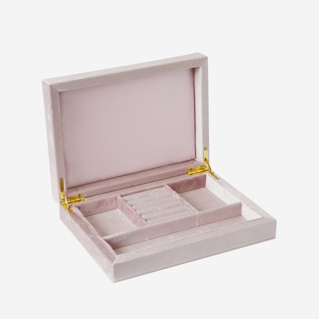 Open pink velvet jewelry box with compartments and gold hinges on an off white background
