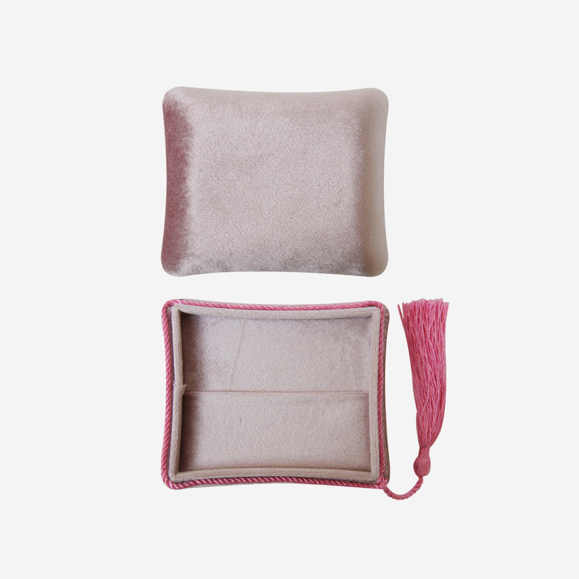 Open pink velvet jewellery box with tassel detail on an off white background