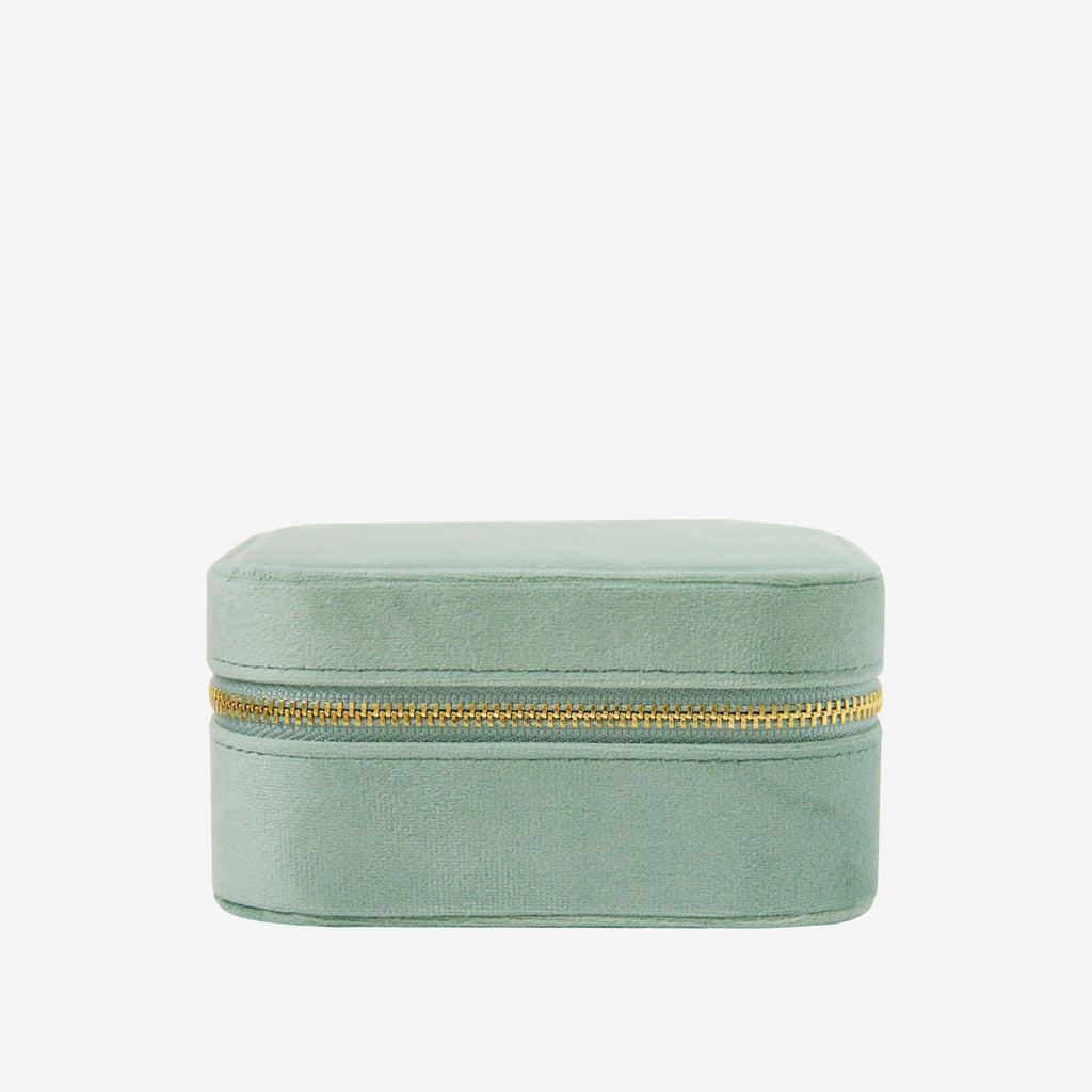 Closed green velvet travel jewelry box with a gold zipper on an off white background