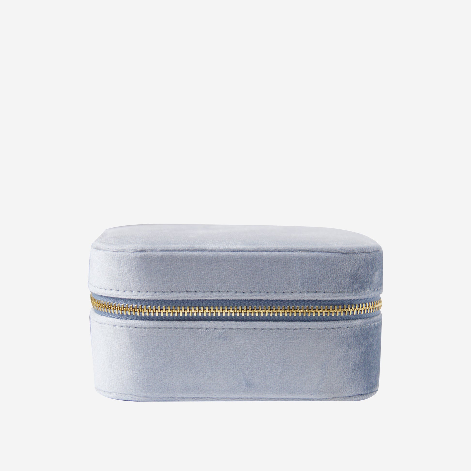 Closed blue velvet travel jewelry box with a gold zipper on an off white background