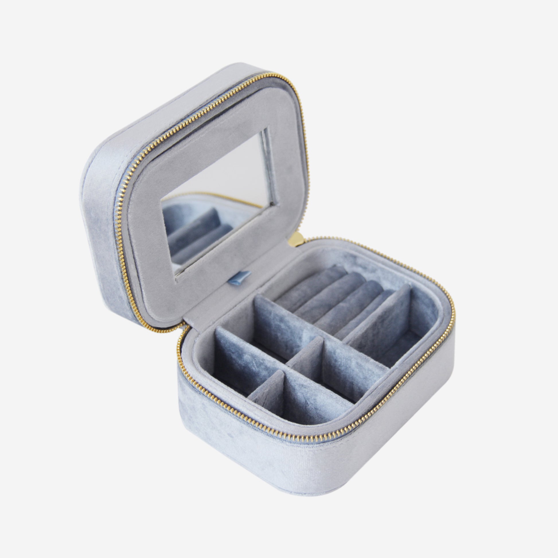 Blue velvet travel jewelry box with compartments  and a mirror on an off white background