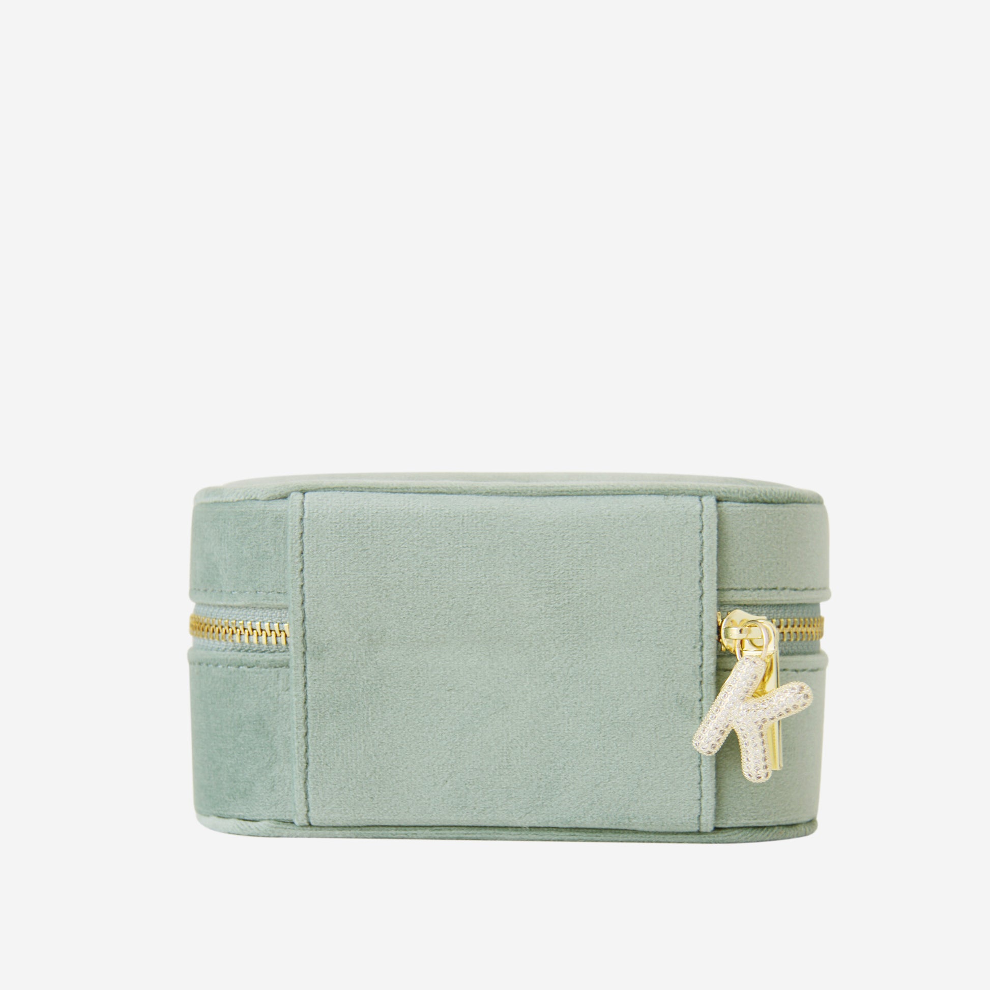 Green velvet travel jewellery box with gold zipper and a crystal and gold letter K charm on an off white background