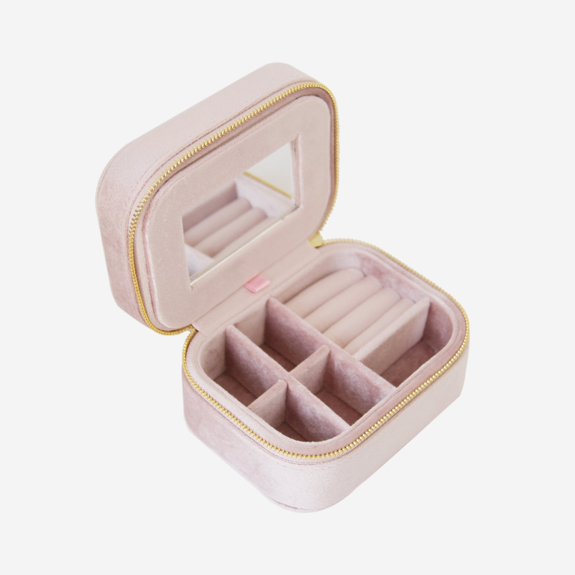 Pink velvet travel jewelry box with compartments and a mirror on an off white background