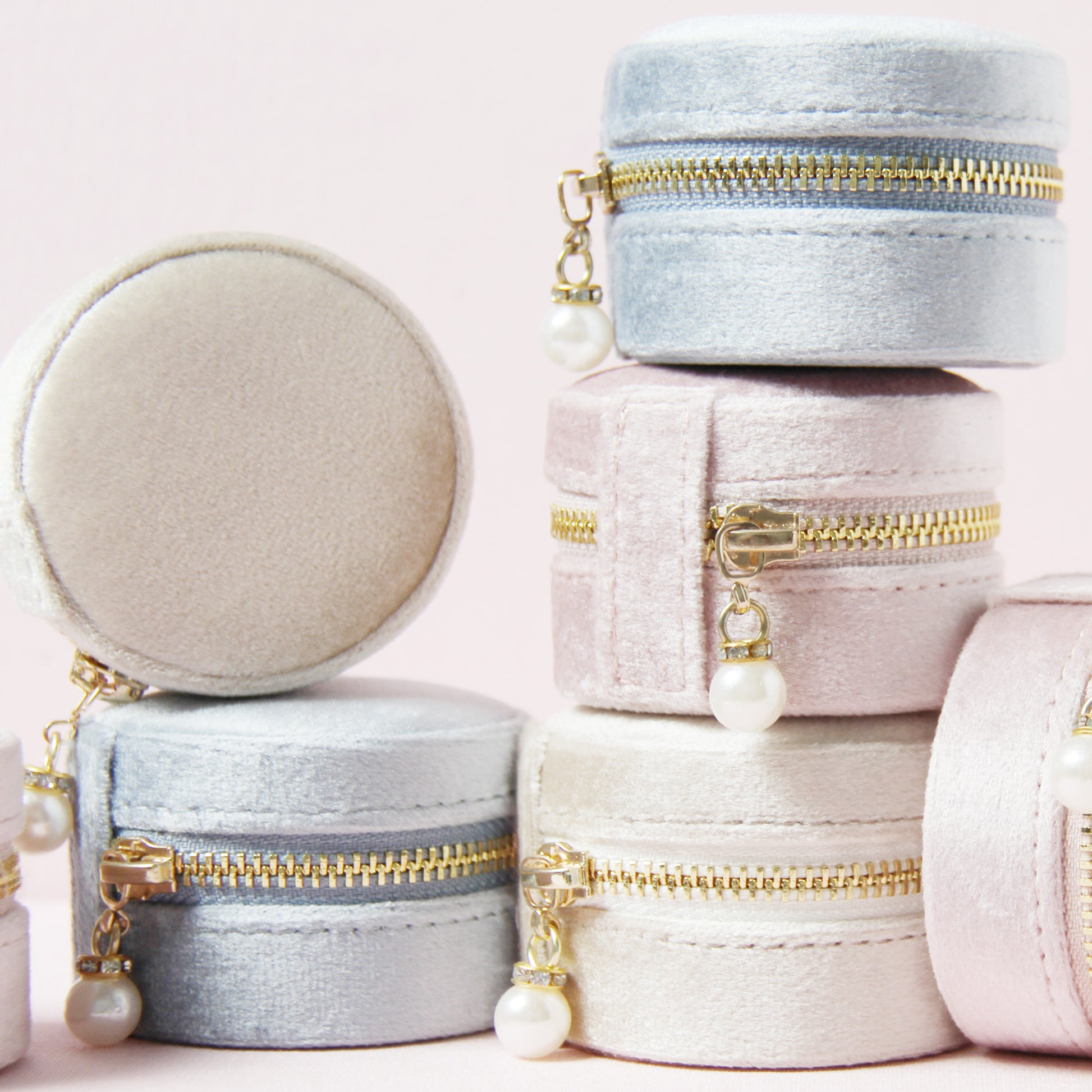 Set of small round velvet jewelry boxes with gold zippers and pearl charms on a light pink background