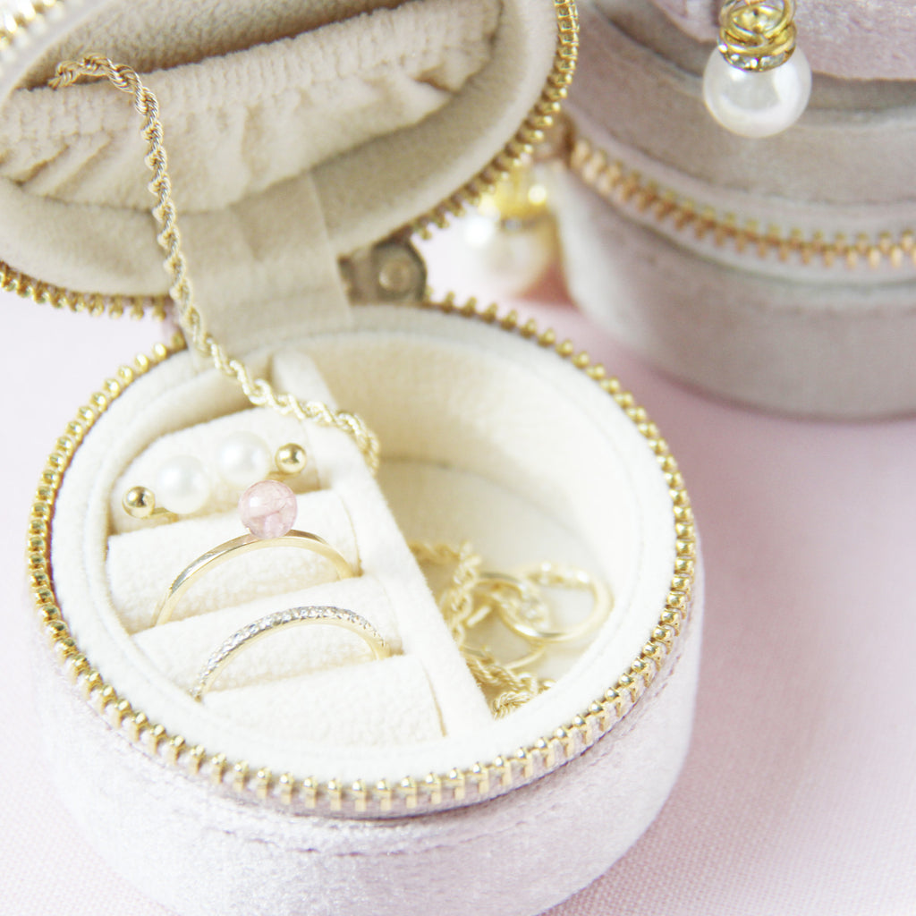Set of small round velvet jewelry boxes with gold zippers and pearl charms on a light pink background