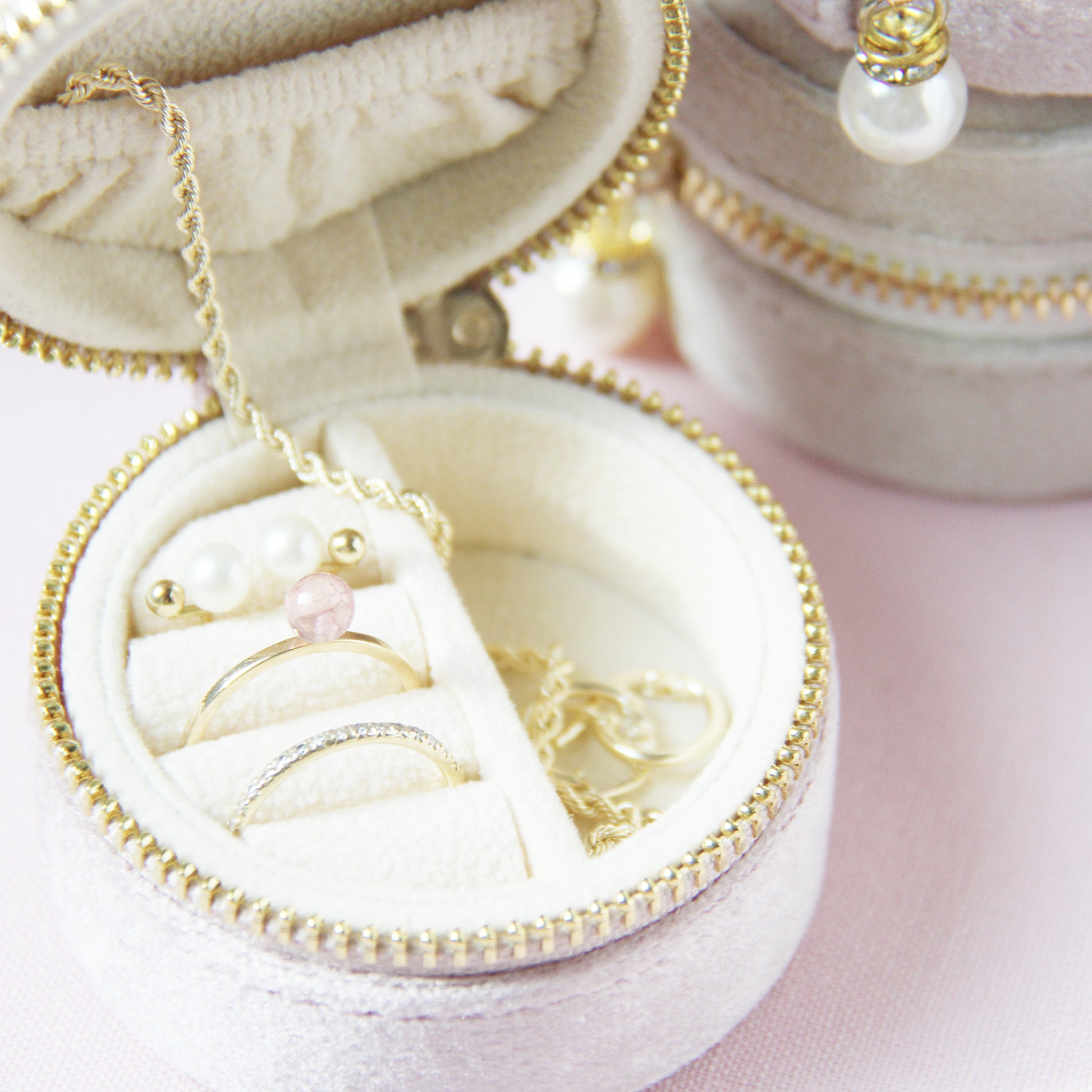 Set of small round velvet jewelry boxes with gold zippers and pearl charms on a light pink background