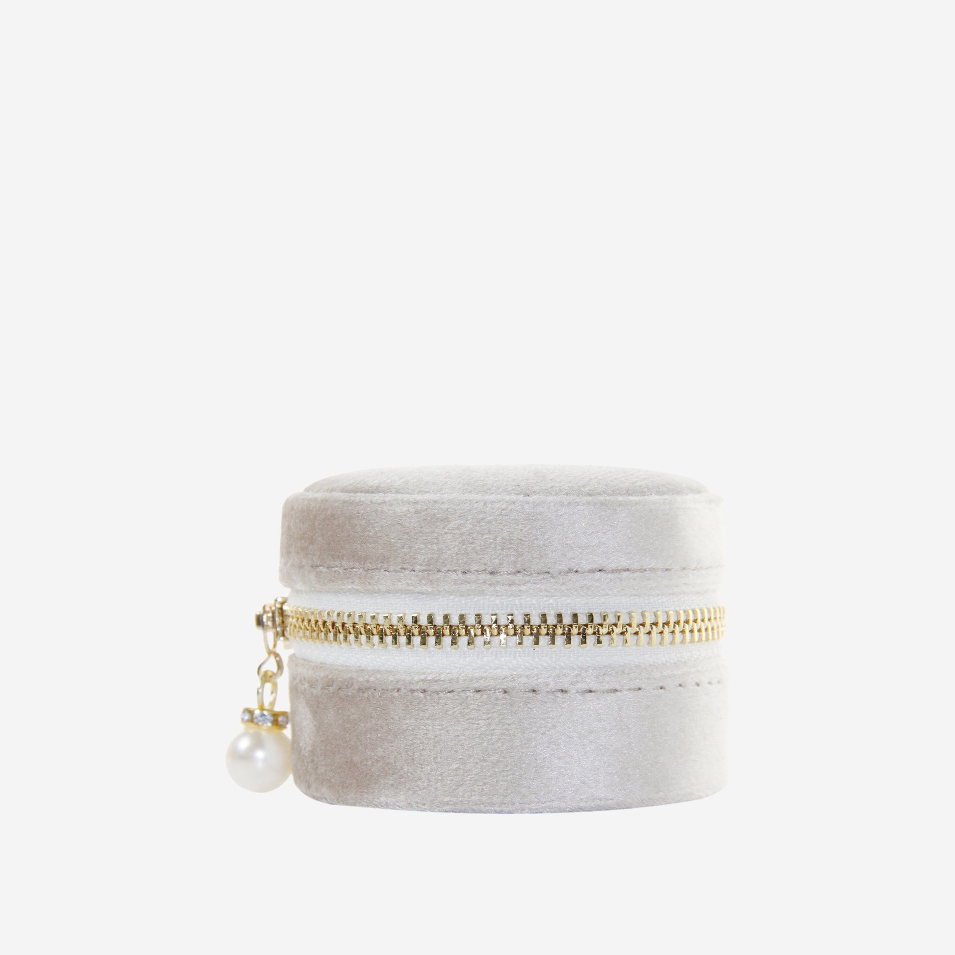 Small round champagne velvet jewelry box with gold zipper and pearl charm on an off white background