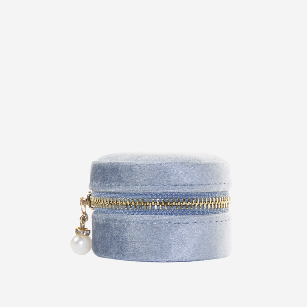 Small round blue velvet jewelry box with gold zipper and pearl charm on an off white background