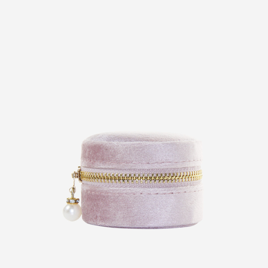 Small round pink velvet jewelry box with gold zipper and pearl charm on an off white background