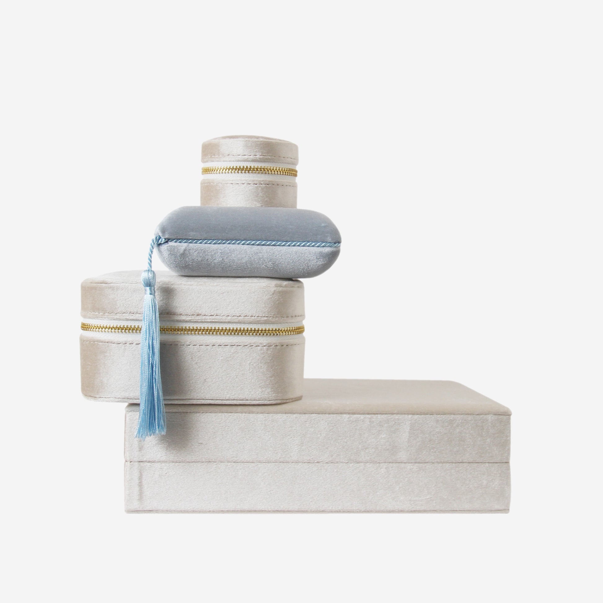 Stack of  3 champagne and 1 blue velvet jewellery boxes of different shapes and sizes on an off white background